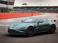 Een gestroomlijnde Aston Martin Vantage F1 Edition staat geparkeerd op een racecircuit, met zitplaatsen op de tribune zichtbaar op de achtergrond.