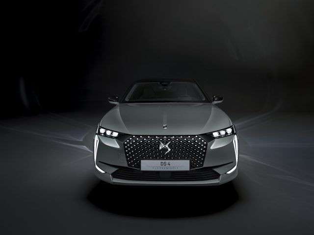 Een zilveren DS 4 La Première-auto wordt van voren getoond tegen een donkere achtergrond. De auto is voorzien van strakke koplampen en een opvallend grille-ontwerp.