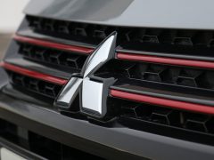 Close-up van de grille van een Mitsubishi-auto, met het logo van het merk met opvallende rode accenten op de horizontale balken.