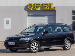 Een strakke zwarte Opel Astra stationwagon staat geparkeerd voor een gebouw waar trots het Opel-bord staat afgebeeld.