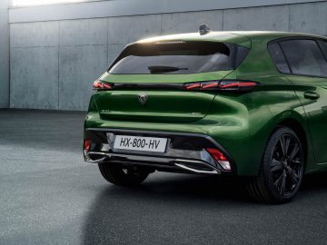 Achteraanzicht van een groene Peugeot 308 geparkeerd op een donkere stoep, met de kentekenplaat HX-800-HV en een modern achterlichtontwerp tegen een achtergrond van een betonnen muur.