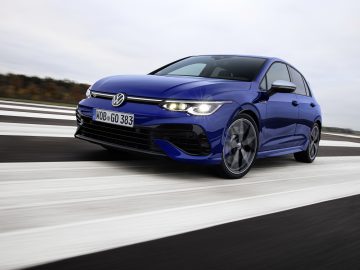 Een blauwe Volkswagen Golf R-auto rijdt op een steeds breder wordende gestreepte weg onder een bewolkte hemel.