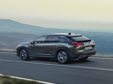 Een donkergrijze Citroën C5 X SUV rijdt op een bochtige weg met een bergachtig landschap op de achtergrond.