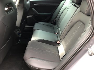 Binnenaanzicht van de achterbank van een Cupra Leon e-Hybrid met zwart lederen bekleding, twee hoofdsteunen en veiligheidsgordels. De achterdeuren en de passagiersstoel zijn zichtbaar.