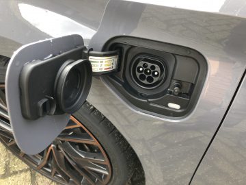 Close-up van de oplaadpoort van een Cupra Leon e-Hybrid met het deksel open, waardoor de connectorsleuven aan de binnenkant zichtbaar zijn.