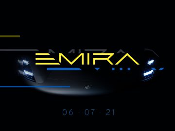 Een auto met verlichte koplampen wordt tentoongesteld in een donkere omgeving. De tekst "Emira" wordt hierboven prominent weergegeven met de datum "06.07.21" eronder, wat verwijst naar de nieuwste Lotus-release.