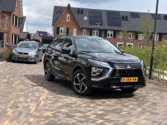 Een zwarte Mitsubishi Eclipse Cross SUV geparkeerd op een stenen oprit in een moderne woonwijk met een andere auto en huizen op de achtergrond.