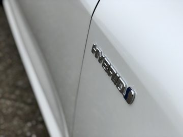 Close-up van een witte Suzuki Swace met het woord 'HYBRID' op de zijkant geschreven.