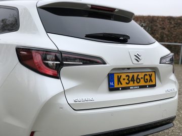 Een witte Suzuki Swace met een Europees kenteken met de tekst K-346-GX staat buiten geparkeerd. De achterkant van de auto toont het Suzuki-logo en de achterlichten.