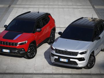 Twee Jeep-SUV's, waaronder een strakke Jeep Compass, staan naast elkaar geparkeerd op een verharde ondergrond. De ene heeft een opvallend rood en zwart kleurenschema, terwijl de andere schittert in zilver en zwart.