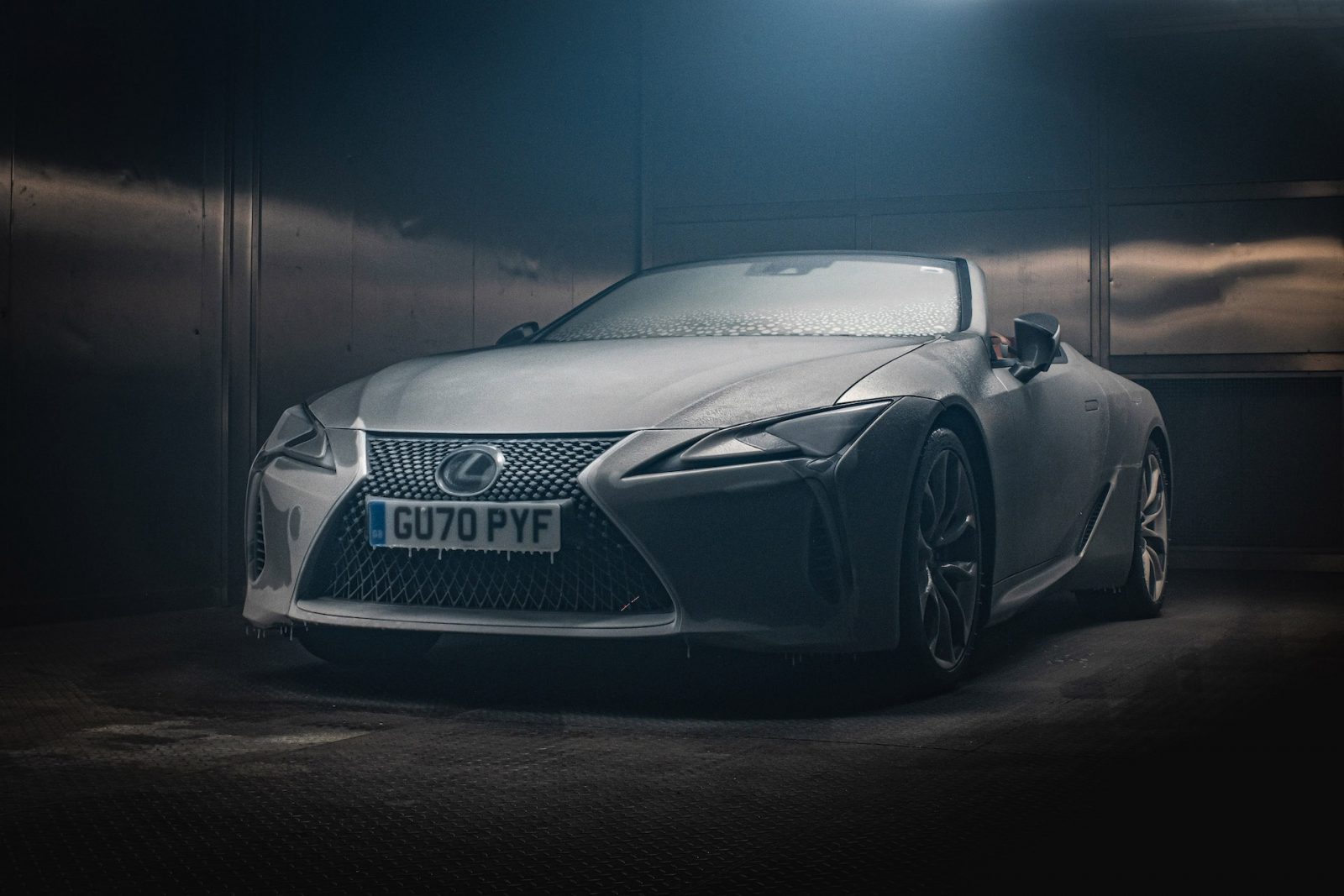 Een zilveren Lexus LC-cabriolet staat geparkeerd in een slecht verlichte garage, met de voorkant en de bestuurderszijde zichtbaar, met kenteken "GU70 PYF.