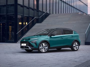 Een groene Hyundai Bayon SUV staat geparkeerd voor een modern glazen gebouw met grote buitentrappen.