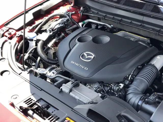 Motorruimte van een Mazda CX-5-voertuig met een Skyactiv-D-dieselmotor, met de afgedekte motoronderdelen en verschillende slangen en aansluitingen.