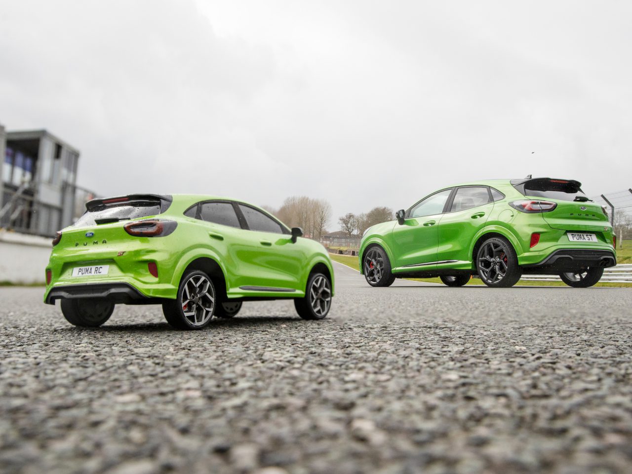 Twee groene compacte SUV's op een verharde ondergrond; de ene op de voorgrond is een op afstand bestuurbaar model en de andere op de achtergrond is een Ford Puma ST op ware grootte.
