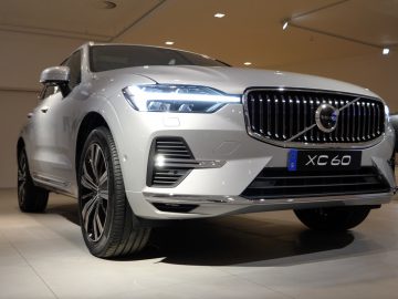 Een slanke zilveren Volvo XC60 SUV wordt tentoongesteld in een goed verlichte binnenomgeving, waarbij de kenmerkende grille en LED-koplampen worden geaccentueerd.