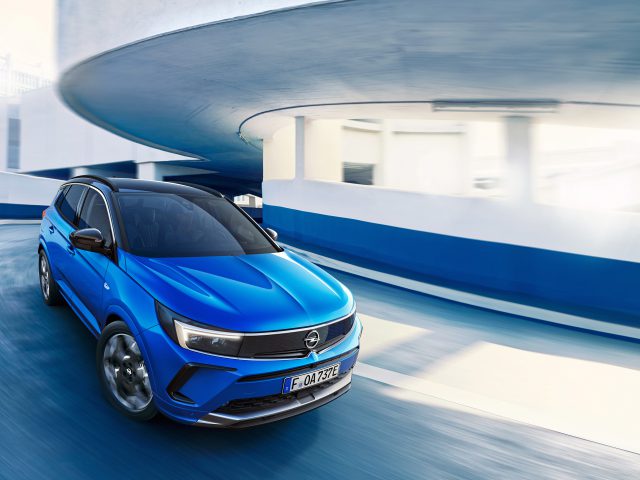 Een blauwe Opel Grandland SUV rijdt door een blauw-witte parkeergarage met meerdere niveaus.