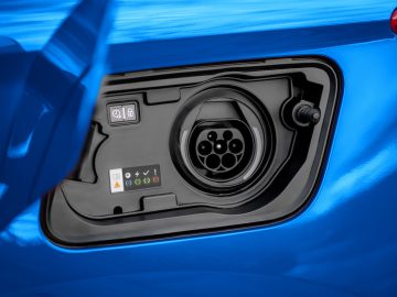 Close-up van de oplaadpoort van een elektrisch voertuig, geïntegreerd in de carrosserie van een blauwe Opel Grandland, met verschillende pictogrammen en symbolen die de laadstatus en poortspecificaties aangeven.