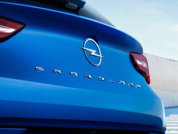 Close-up van de achterkant van een Opel Grandland, met het logo van het blauwe voertuig en de modelnaam in chromen letters, terwijl het achterlicht aan de linkerkant zichtbaar is.