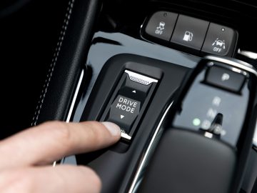 Een close-up van de hand van een persoon die op de knop 'Drive Mode' drukt op de middenconsole van een Opel Grandland. De knop wordt omringd door diverse andere bedieningselementen en de versnellingspook.