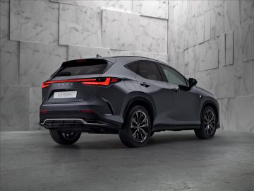 Een donkergekleurde Lexus NX 450h+, gezien vanuit de achterhoek, staat geparkeerd in een moderne binnenruimte met een marmeren muurachtergrond.