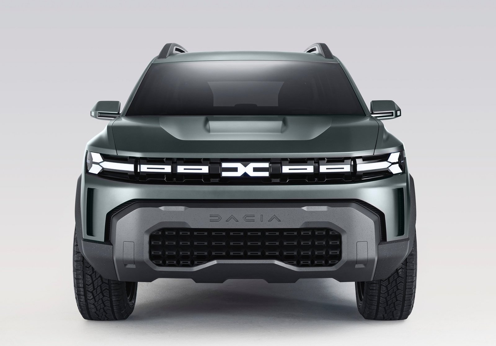 Vooraanzicht van een groene Dacia SUV met opvallende, futuristische designelementen, waaronder een prominente grille en hoekige koplampen. Het voertuig heeft een moderne en robuuste uitstraling.