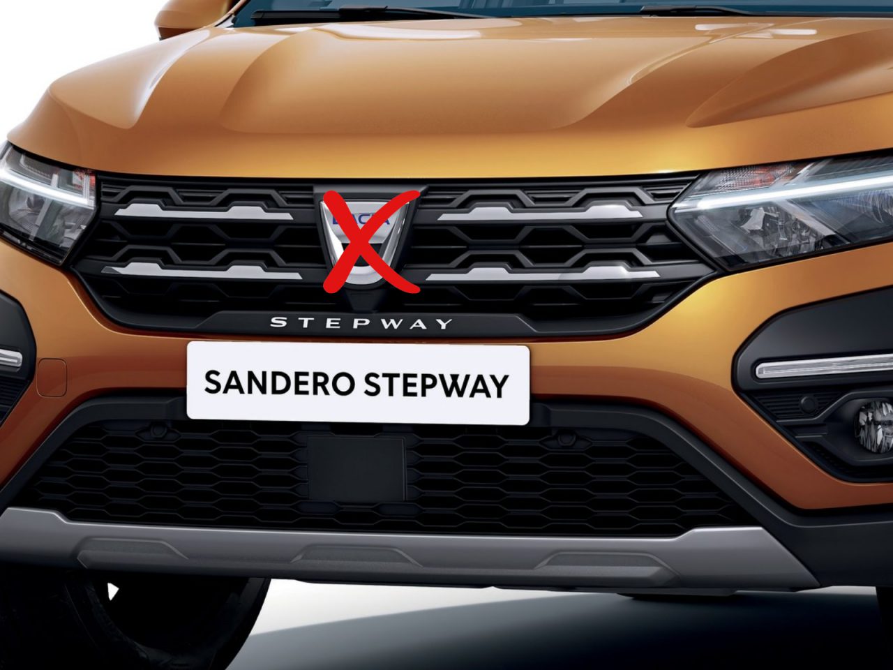Close-up van de grille en bumper van een oranje Renault Sandero Stepway met een rood kruis boven het Renault-logo, waardoor de designwortels van Dacia zichtbaar worden.