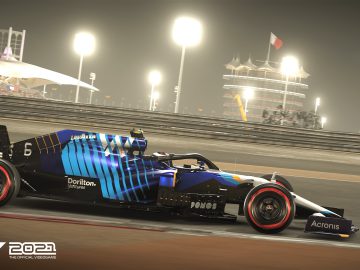 Een Formule 1-auto racet 's nachts op een circuit, verlicht door de gloeiende tribune en de iconische verkeerstoren van het Bahrain International Circuit. Linksonder wordt "F1 2021 The Official Videogame" weergegeven.