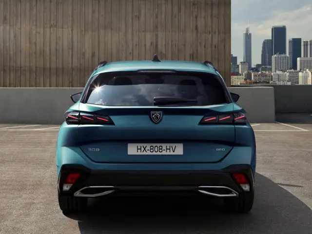 Achteraanzicht van een blauwe Peugeot 308 SW hatchback geparkeerd in een stedelijke omgeving, met kenteken HX-808-HV en stadsbeeld met wolkenkrabbers op de achtergrond.
