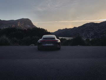 Een laag hoekaanzicht van een geparkeerde Porsche 911 GT3 Touring vanaf de achterkant, tegen een adembenemende achtergrond van bergen en een vallei tijdens zonsondergang.