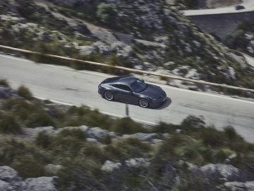 Een strakke Porsche 911 GT3 Touring rijdt over een bochtige bergweg met rotsachtige hellingen en schaarse begroeiing.