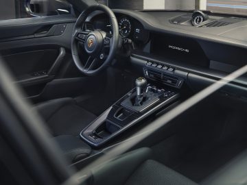 Binnenaanzicht van een Porsche 911 GT3 Touring-sportwagen met het strakke dashboard, het stuur, de versnellingspook en het bedieningspaneel.