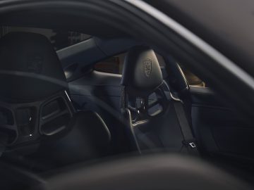 Interieur van een luxe sportwagen, met de nadruk op de zwartleren kuipstoelen met een opvallend logo op de hoofdsteunen. De afbeelding toont het strakke en moderne ontwerp van het interieur van de Porsche 911 GT3 Touring.