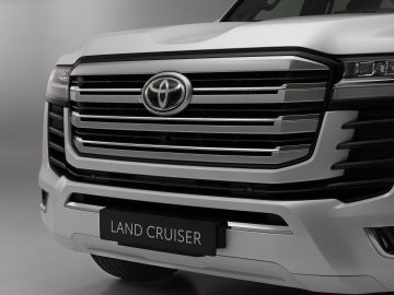 Close-up van de grille en een deel van de koplamp van een smetteloos witte Toyota Land Cruiser, met het embleem en het naamplaatje duidelijk zichtbaar.