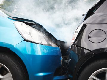 Twee auto's, de ene blauw en de andere zwart, waren betrokken bij een frontale botsing, waarbij rook uit het botsgebied kwam. De schade suggereert dat beide voertuigen nu als sloepauto kunnen worden beschouwd en waarschijnlijk niet de moeite waard zijn voor reparaties.