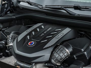 Close-up van een BMW Alpina V8 BiTurbo-motor onder de motorkap, die het precisievakmanschap laat zien. Op de motorkap zijn zowel het BMW- als het Alpina-logo prominent aanwezig, wat ongeëvenaarde prestaties symboliseert.