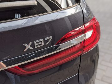 Close-up van de achterhoek van een donkergekleurde BMW Alpina-auto, met het achterlicht en het embleem "XB7" op de kofferbak.
