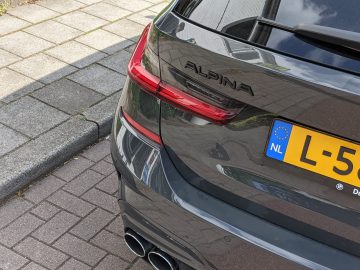 Close-up van de achterkant van een donkergekleurde BMW Alpina-auto, geparkeerd op straat, met de achterlichten en het Nederlandse kenteken.