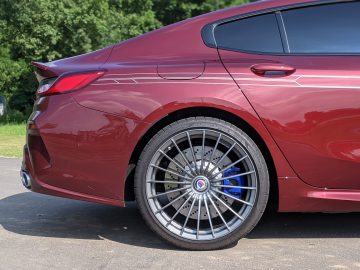 Close-up van de achterkant en het stuur van een rode BMW Alpina met opvallende zilverkleurige lichtmetalen velgen en krijtstreepdetail.