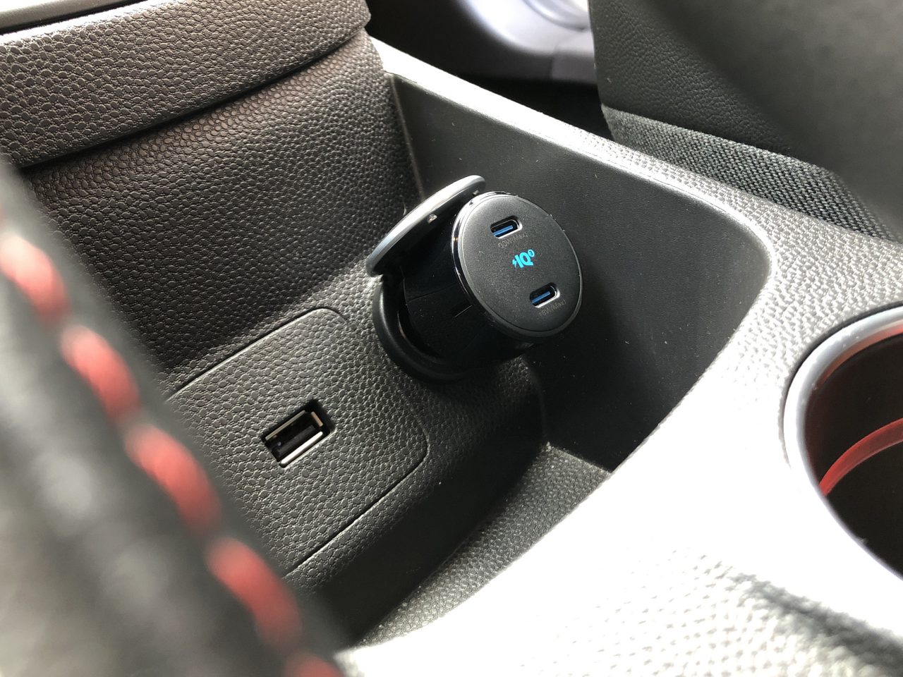 Een Anker PowerDrive+ III Autolader wordt aangesloten op de sigarettenaanstekeraansluiting in de middenconsole van een voertuig. Een andere USB-poort bevindt zich in de buurt.