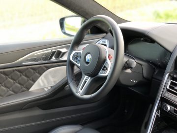 Binnenaanzicht van de BMW M8 Gran Coupé Competition, met het luxueuze stuurwiel met BMW-logo, een strak dashboard en een deurpaneel versierd met gewatteerde lederen details.