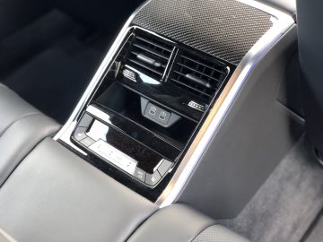 Close-up van de middenconsole achterin in de BMW M8 Gran Coupé Competition, met ventilatieopeningen voor de airconditioning, USB-oplaadpoorten en knoppen voor klimaatregeling. De console is zwart met metallic accenten.