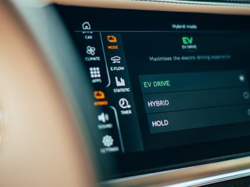 Close-up van het dashboardscherm van een auto met verschillende rijmodi, waaronder EV Drive, Hybrid en Hold. Het scherm toont opties om de elektrische rijervaring in de Lotus Emira te maximaliseren.