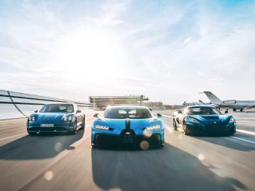 Drie sportwagens, waaronder een strakke Bugatti en een krachtige Rimac, rijden op een landingsbaan van een luchthaven met een privéjet op de achtergrond onder een heldere hemel.