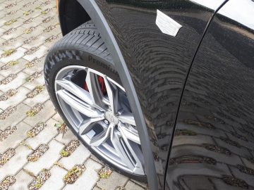 Een close-up van de voorband en het wiel van een zwarte Cadillac XT4. De afbeelding toont het loopvlakpatroon van de band, het ontwerp van de lichtmetalen velgen en een klein deel van de zijkant van het voertuig, met het Cadillac-logo zichtbaar boven de wielkast.