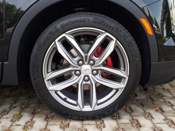 Close-up van het voorwiel van een Cadillac XT4 met een Continental-band en een velg van zilverlegering, geparkeerd op een geplaveide ondergrond. De remklauw is rood zichtbaar achter de velg.