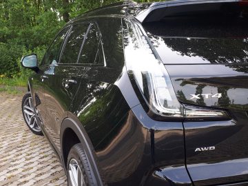 Een glanzend zwarte Cadillac XT4 AWD SUV, met het opschrift 'XT4 AWD', geparkeerd op een geplaveid oppervlak met bomen op de achtergrond.