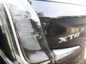 Close-up van het achterlicht linksachter en het XT4-embleem van een zwarte Cadillac XT4, die de omgeving perfect weerspiegelt en de elegantie van de Cadillac XT4 laat zien.