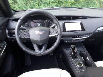 Binnenaanzicht van een moderne Cadillac XT4 met een stuur met bedieningsknoppen, een digitaal dashboard, een aanraakscherm en een versnellingspook. De stoelen zijn wit met zwarte accenten.