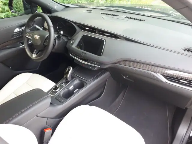 Interieur van een moderne Cadillac XT4 met het dashboard, het stuur, de middenconsole met bekerhouders, de versnellingspook en een aanraakscherm. Zwart en beige bekleding.