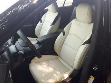 Binnenaanzicht van een Cadillac XT4 met de voorstoelen met lichtbeige bekleding, een zwart dashboard en een middenconsole. Aan de linkerkant is een gedeelte van de bestuurdersdeur zichtbaar.